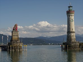 Lion statue and lighthouse with clear sky and calm water, nearby town and mountains in the