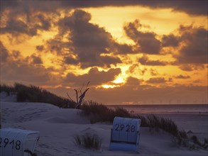 Beach chairs on the beach at sunset, with impressive clouds in the sky and dunes in the background,