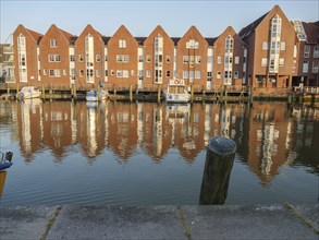 Brick houses are reflected in the calm waters of a canal, jetties and boats are visible, husum,