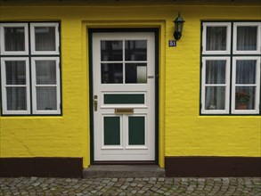 A yellow house with a green and white door and white windows, Eckernforde, Schleswig-Holstein,