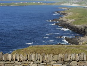 View over the sea and a stone wall to green fields and waves, Lerwick, Shetlands, Scotland, United