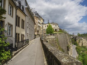 Historic city wall with path and historic buildings under a cloudy sky, Luxembourg City,