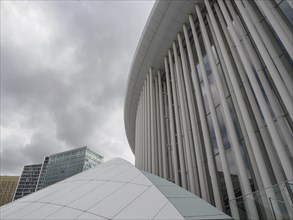 Modern building with white façade and glass windows in front of skyscrapers and clouds, Luxembourg