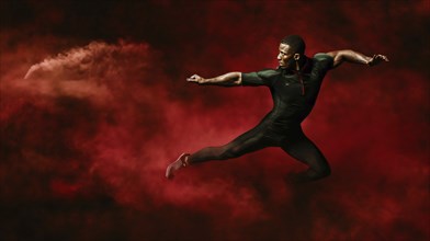 A male athlete leaps through a cloud of red smoke against a dark background, emphasizing power and
