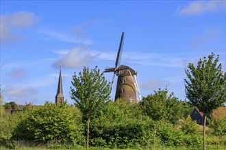 Landscape with windmill and church tower, surrounded by green trees and blue sky, bredevoort,