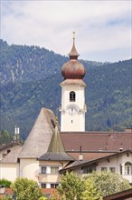 Church with high bell tower in a traditional alpine village, surrounded by mountains and many