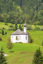 A small white church on a hill with green meadows and dense forests in the background, Achernsee,