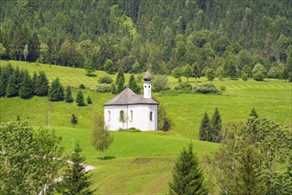 A small white church on a grassy hill surrounded by lush green meadows and trees, Achernsee,