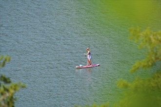 Person stand-up paddling on a green lake surrounded by nature, Achernsee, Austria, Germany, Europe