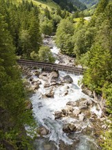 Wooden bridge over a wild river in a forest, with rocks and flowing water, Zillertal, Austria,