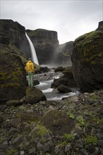 Young man with yellow jacket standing in front of waterfall, Haifoss and Granni waterfall at a