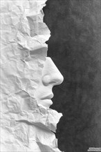 Side view of a human face carved out of crumpled paper with high contrast between black and white,