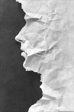 Profile of a face crafted from torn and crumpled paper against a dark background, featuring an