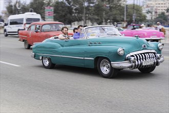 Havana, Cuba, Central America, A green vintage car drives along the road amidst the city traffic,