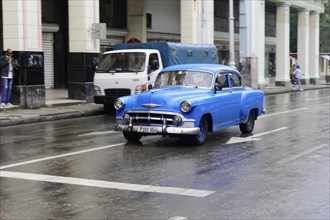 Havana, Cuba, Central America, Blue vintage car drives on wet road in the city, Central America