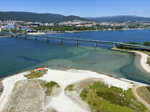 View of a coastal town with a bridge over a river flowing into the ocean, surrounded by hills and