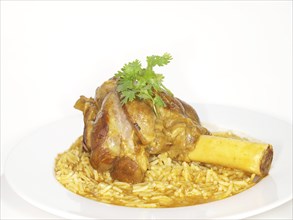 Lamb shank in juicy yellow rice, on white plate towards white