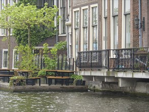 Urban canal with neighbouring buildings and metal balcony balustrades, next to tables and chairs by