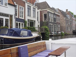 A boat moored in front of a row of townhouses on the canal on a calm, cloudy day, windows with