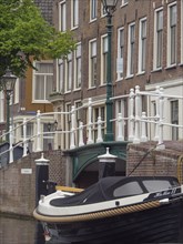 An elegant boat moored by a bridge, surrounded by historic city buildings and lanterns on a canal,