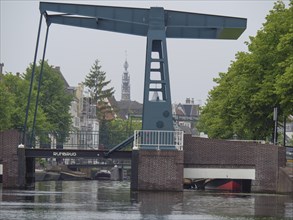 A bascule bridge over a canal with a church tower in the background and tree-lined streets, Leiden,