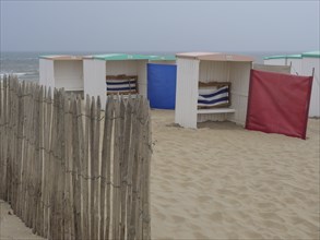 Beach huts on a sandy beach with wooden fence and sun protection in front of the ocean, Leiden,