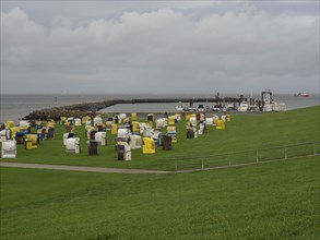 Many beach chairs scattered on a green meadow by the sea, a harbour and cloudy sky in the