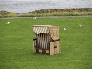 A single beach chair on a green meadow near the sea, surrounded by birds, cuxhaven, germany