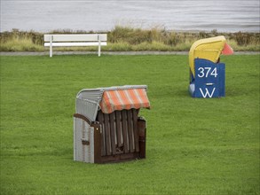 A single beach chair and a bench stand on a green meadow by the sea, cuxhaven, germany