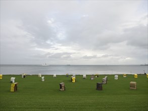 Colourful beach chairs stand in a meadow on the coast, the sky is cloudy, cuxhaven, germany