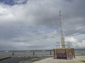 A radio mast on a brick base by the sea under a cloudy sky, cuxhaven, germany