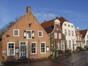 Traditional houses with red tiled roofs and cobblestone streets under a clear blue sky, Greetsiel,