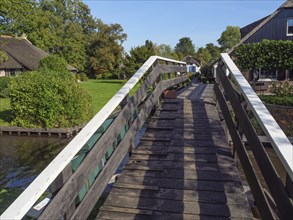 View along a wooden bridge over a canal in a green village on a sunny day, giethoorn, the