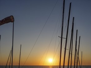 Sunset over the sea with silhouettes of sailboat masts in a peaceful atmosphere, De Haan, Flanders,
