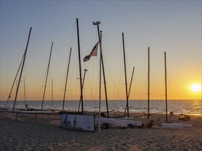 Boats with masts on the beach at sunset, calm atmosphere, warm light and sea in the background, De