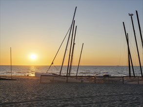 Beach with boat masts at sunset, calm and peaceful atmosphere, sand and sea, warm colours, De Haan,