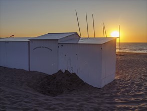White painted beach huts on the beach at sunset with calm sea and sandy bottom, De Haan, Flanders,