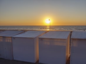 Sunset over the sea, beach with white huts, quiet and peaceful atmosphere with a warm light, De