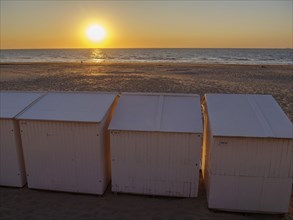 Sunset on the beach with white huts, empty sandy area and calm atmosphere, sea in the background,