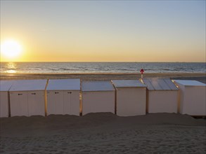 Beach with white huts, sunset over the sea, warm orange colours and calm atmosphere, De Haan,