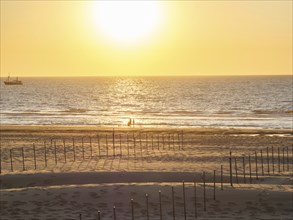 People on the beach at sunset, with a ship in the background, De Haan, Flanders, Belgium, Europe