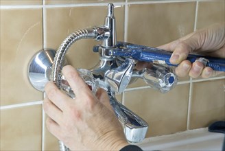 Hands of a plumber with wrench fixing a tap