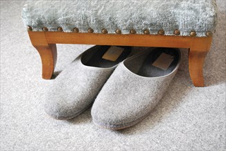 Old grey slippers on carpet with stool