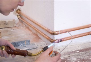 Hand of a plumber with soldering iron and copper pipes