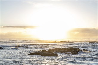 Sunrise over the sea with gentle waves. Sandy beach with lava rocks and blue water alternating with