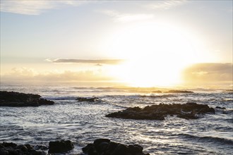 Sunrise over the sea with gentle waves. Sandy beach with lava rocks and blue water alternating with