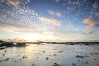 Sunrise over the sea with gentle waves. Sandy beach with lava rocks and blue water alternating with