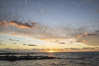 Sunrise over the sea with gentle waves. Sandy beach with lava rocks and blue water alternating with