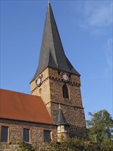 Historic church with a high tower and visible bells. Traditional architecture under a blue sky,