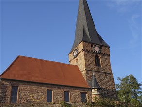Historic church with high tower and bells. Brick walls with a red roof under a clear sky, Kandel,